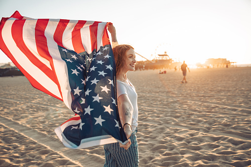 Adolescent woman enjoying a sunset in Santa Monica (California) holding a US flag