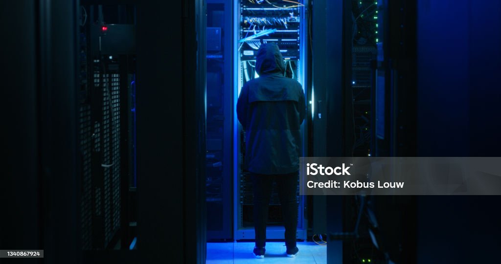 Shot of a hacker walking through a server room Always ensure that your data is secure Criminal Stock Photo