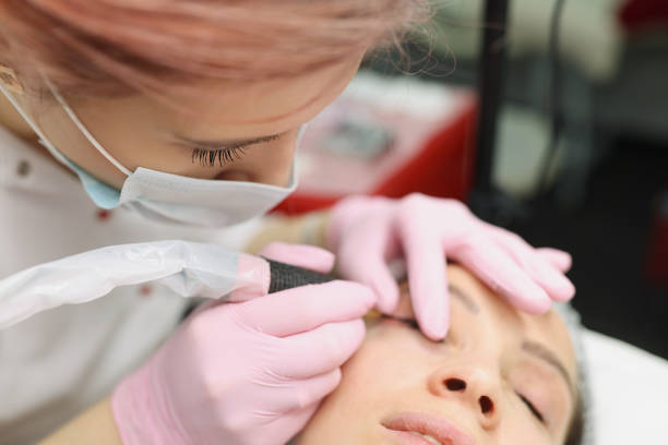 istock Master in protective medical mask making permanent eye makeup to client in beauty salon 1340869078