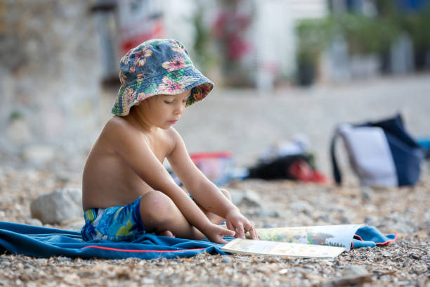 istock Cute blond toddler boy, reading a book on the beach 1340871080