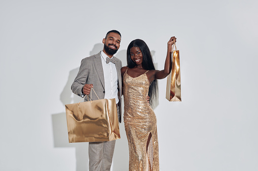 Beautiful African couple carrying gold colored shopping bags and smiling while  standing against gray background