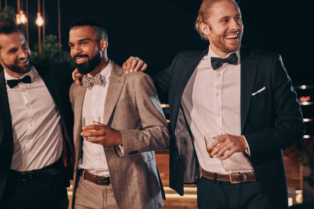 drei gutaussehende männer in anzügen, die sich verbinden und whisky trinken - elegante kleidung stock-fotos und bilder