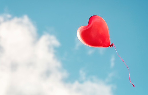 Red heart shaped balloon flying in a blue sky background