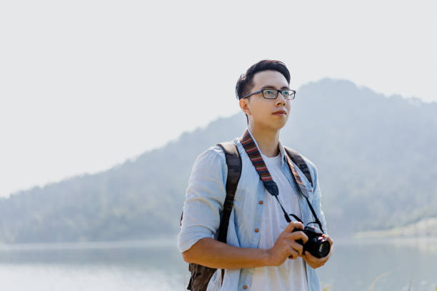 istock Young asian backpacker with camera at scenic lakeside 1340875391