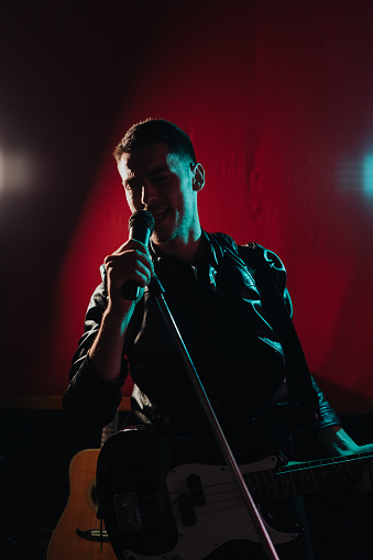 Rock band vocalist with the guitar singing to microphone in lights on red background