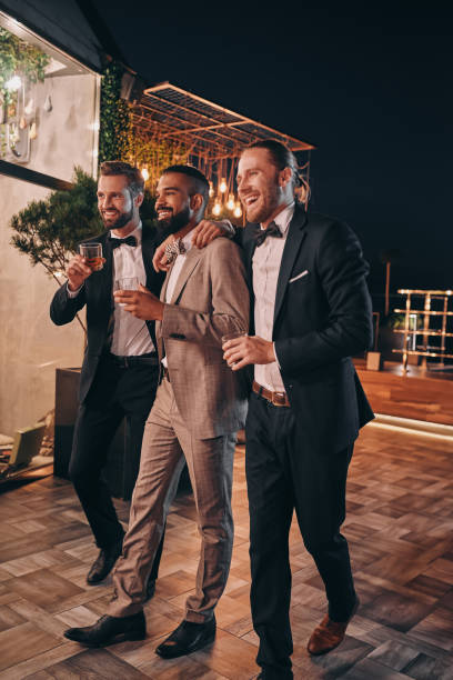 pełna długość trzech przystojnych mężczyzn w garniturach i muszkach pijących whisky i komunikujących się - people formalwear vertical full length zdjęcia i obrazy z banku zdjęć