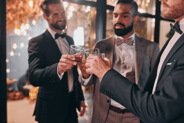 istock Three handsome men in suits toasting with whiskey and smiling 1340877355