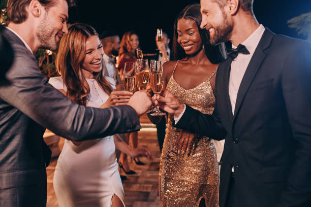 grupo de personas en ropa formal brindando con champán y sonriendo - formal fotografías e imágenes de stock