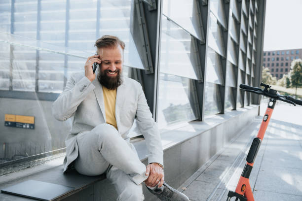 smiling senior business man sitting outdoors on wall talking at mobile