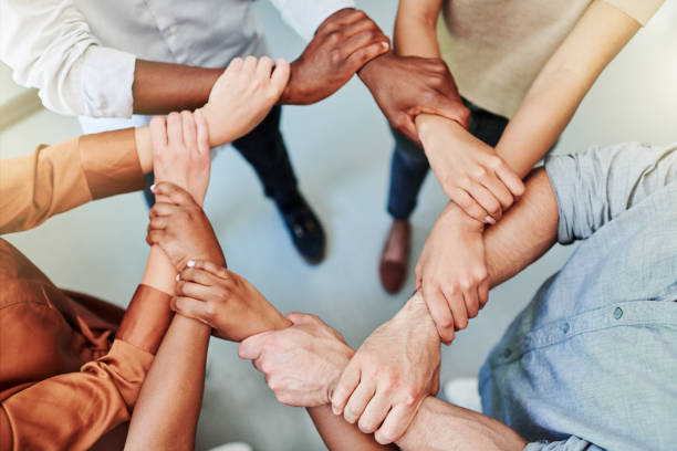 High angle shot of a group of businesspeople holding one another's wrists in a circular formation stock photo