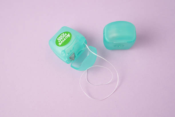 istock Dental mint floss in a small blue container. Small dental floss container on violet background 1340883300
