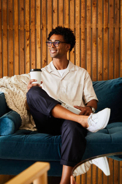 istock Smiling young African American designer drinking coffee on an office sofa 1340884667