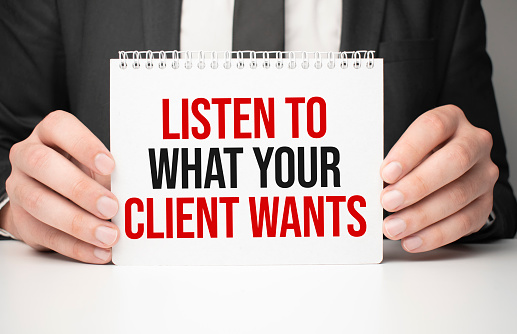 Businessman holding sheet of paper with a message LISTEN TO WHAT YOUR CLIENT WANTS