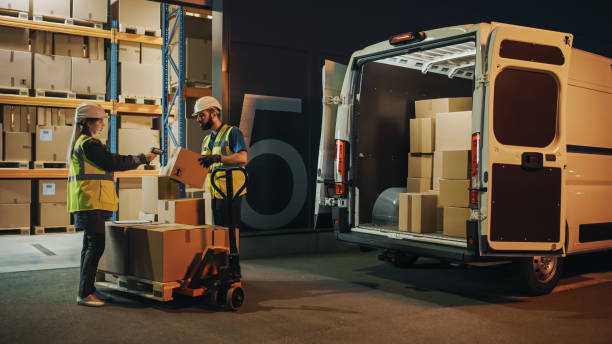 istock Outside of Logistics Retail Warehouse: Manager Using Tablet Computer and Scanner, talking to Worker Loading Delivery Truck with Cardboard Boxes, Online Orders, Medicine Supply, E-Commerce. Evening 1340887503
