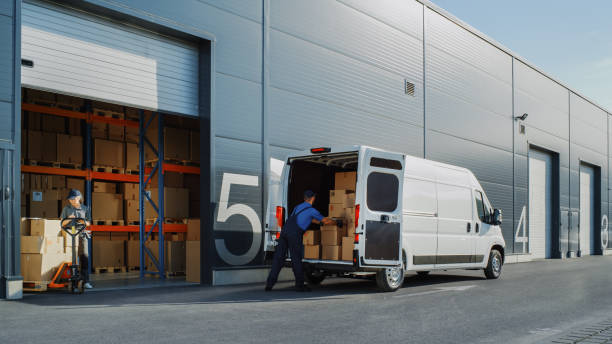 istock Outside of Logistics Retailer Warehouse With Female Manager Using Tablet Computer, Worker Loading Delivery Truck with Cardboard Boxes. Online Orders, Purchases, E-Commerce Goods, Merchandise 1340887505