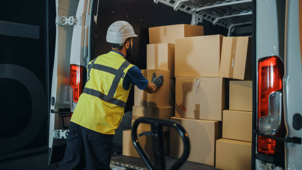 Handsome Latin Male Worker Wearing Hard Hat Loads Cardboard Boxes into Delivery Truck. Delivering Online Orders, E-Commerce Goods, Food, Medicine Supply. Overworked Tired Frontline Hero Doing Job Handsome Latin Male Worker Wearing Hard Hat Loads Cardboard Boxes into Delivery Truck. Delivering Online Orders, E-Commerce Goods, Food, Medicine Supply. Overworked Tired Frontline Hero Doing Job logistical stock pictures, royalty-free photos & images