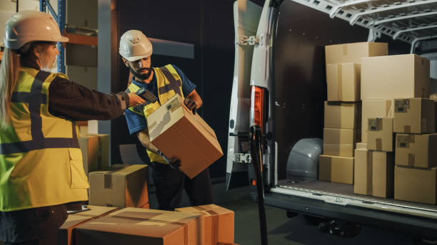 istock Outside of Logistics Retail Warehouse: Manager Using Tablet Computer and Scanner, talking to Worker Loading Delivery Truck with Cardboard Boxes, Online Orders, Medicine Supply, E-Commerce. Evening 1340887525