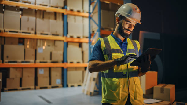 outside of logistics retail warehouse: handsome latin manager using tablet computer for inventory. delivery service with cardboard boxes, online orders, e-commerce. evening shot - logistical imagens e fotografias de stock