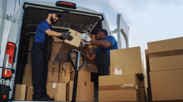 istock Logistics Warehouse Two Happy Workers Talk, Joke use Hand Pallet Truck Start Loading Delivery Truck with Cardboard Boxes, Online Orders, Purchases, E-Commerce Goods. Low Angle 1340887558