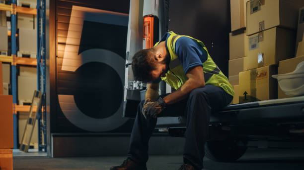 Latin Male Worker Wearing Hard Hat Loads Cardboard Boxes into Delivery Truck, Rests. Online Orders, E-Commerce Goods, Food, Medicine. Tired Overworked Frontline Hero. Dramatic Shot Latin Male Worker Wearing Hard Hat Loads Cardboard Boxes into Delivery Truck, Rests. Online Orders, E-Commerce Goods, Food, Medicine. Tired Overworked Frontline Hero. Dramatic Shot logistical stock pictures, royalty-free photos & images