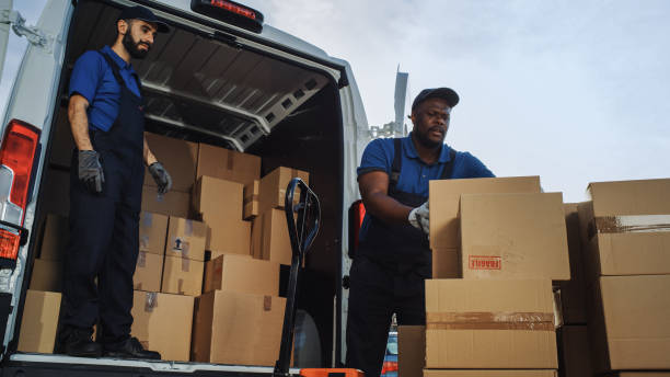 istock Logistics Warehouse Two Happy Workers Talk, Joke use Hand Pallet Truck Start Loading Delivery Truck with Cardboard Boxes, Online Orders, Purchases, E-Commerce Goods. Low Angle 1340887572