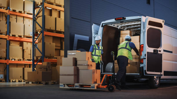 istock Retailer Warehouse Two Happy Workers Talk, Joke use Hand Pallet Truck Start Loading Delivery Truck with Cardboard Boxes, Online Orders, Purchases, E-Commerce Goods. 1340887652