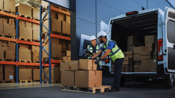 istock Outside of Retailer Distributions Warehouse With Inventory Manager Using Tablet Computer, talking to Worker Loading Delivery Truck with Cardboard Boxes. Online Orders, Purchases, E-Commerce Goods 1340887654