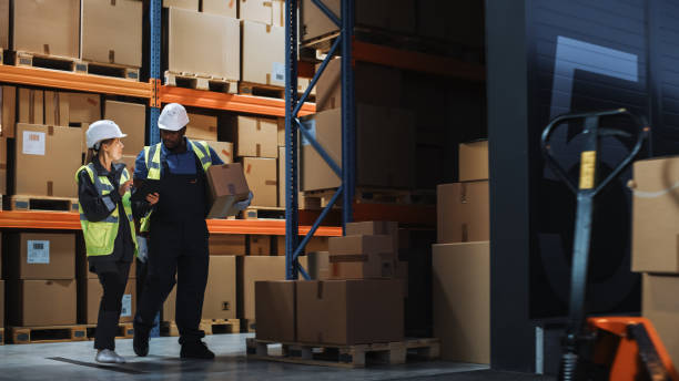 Outside of Logistics Distributions Warehouse: Inventory Manager Using Tablet Computer, talking to Worker with Cardboard Box Walking out of Warehouse. Online Orders, E-Commerce. Outside of Logistics Distributions Warehouse: Inventory Manager Using Tablet Computer, talking to Worker with Cardboard Box Walking out of Warehouse. Online Orders, E-Commerce. logistical stock pictures, royalty-free photos & images