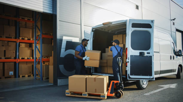 outside of logistics distributions warehouse: two workers talk, joke use hand pallet truck start loading delivery truck with cardboard boxes, online orders, purchases, e-commerce goods. - logistical imagens e fotografias de stock