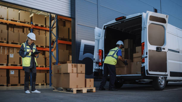 istock Outside of Logistics Distributions Warehouse With Inventory Manager Using Tablet Computer, talking to Worker Loading Delivery Truck with Cardboard Boxes. Online Orders, Purchases, E-Commerce Goods 1340887734
