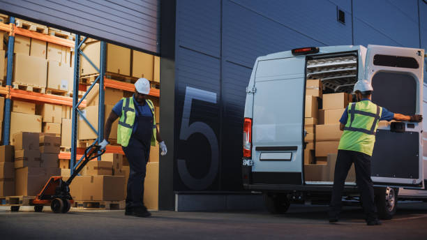 istock Logistics Warehouse Two Happy Workers Talk, Joke use Hand Pallet Truck Start Loading Delivery Truck with Cardboard Boxes, Online Orders, Purchases, E-Commerce Goods. 1340887749