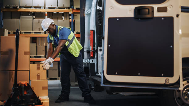 Handsome Black Male Retail Warehouse Worker  Loads Cardboard Boxes in  Delivery Truck. Logistics Retail Center, Delivering e-Commerce Online Orders, Food, Medicine Supply. Handsome Black Male Retail Warehouse Worker  Loads Cardboard Boxes in  Delivery Truck. Logistics Retail Center, Delivering e-Commerce Online Orders, Food, Medicine Supply. logistical stock pictures, royalty-free photos & images