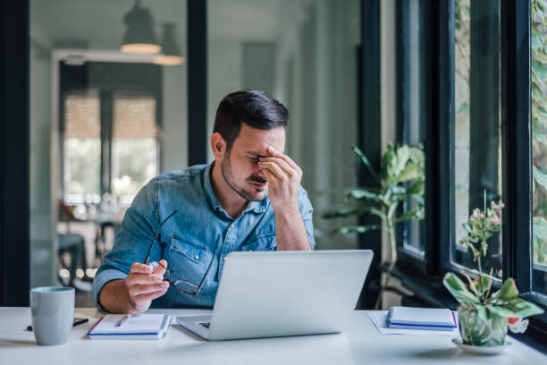 Businessman office working holding sore head pain from desk working and sitting all day using laptop computer or notebook suffering headache sick worker overworking concept