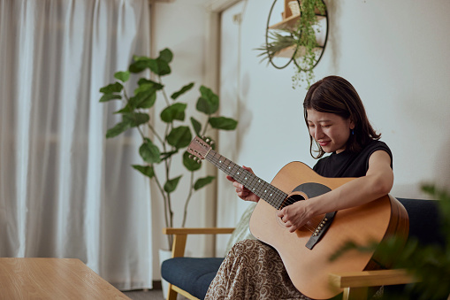 Young Japanese woman playing the guitar in the living room