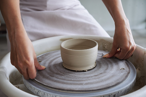 Close-up image of creative young woman cutting off clay pot with wire tool