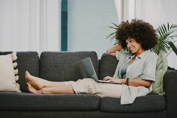 Full length shot of an attractive young woman sitting alone on her sofa at home and using her laptop stock photo