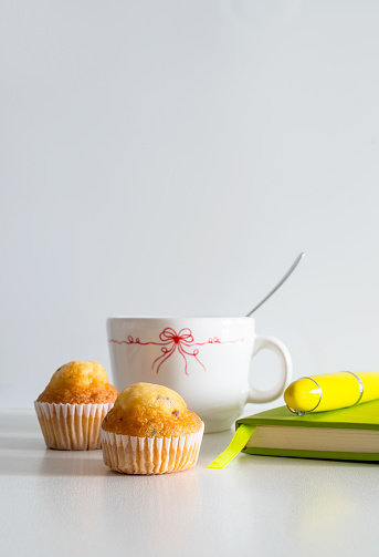 A breakfast to start the day right, consisting of a coffee and two muffins with chocolate with a notebook to take notes and plan the day, on a white background