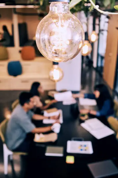 Photo of Shot of a lightbulb hanging over a group of creatives working together