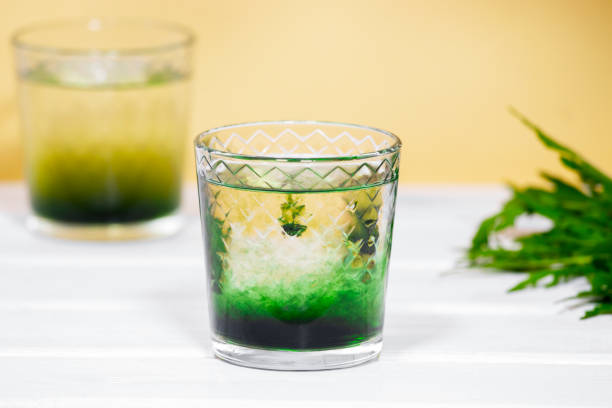 istock Green Chlorophyll or Chlorella drink in glass with water on white table, Orange Background. Green Drops in clear water, Antioxidant food and drinks. 1340902752