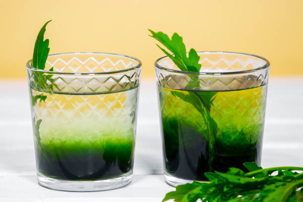 зеленый хлорофилл или хлорелла пить в стакане с водой на белом столе, оранжевый фон. зеленые капли в прозрачной воде, антиоксидантная пища и - chlorophyll стоковые фото и изображения