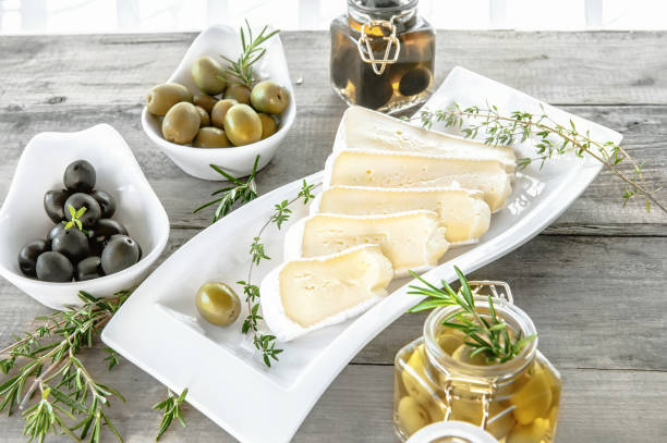 les olives sont vertes et noires avec du fromage à pâte molle avec de la moisissure comme le brie, le camembert à l’huile d’olive et le thym - dishware butter cutting board agriculture photos et images de collection
