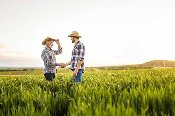 istock Two happy farmers shaking hands on an agricultural field. 1340905736