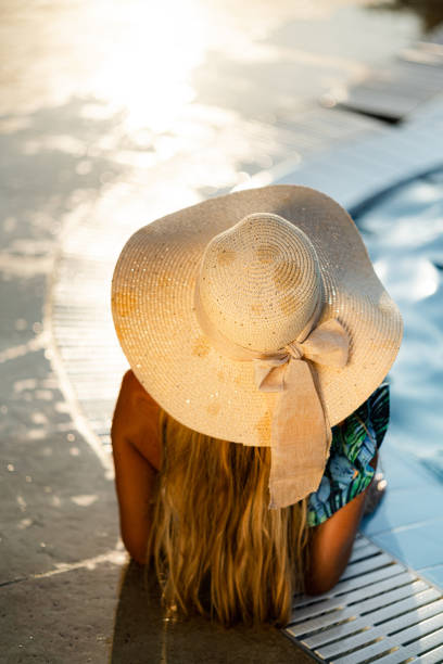 istock Back view of a woman with sun hat looking at view from poolside 1340907955