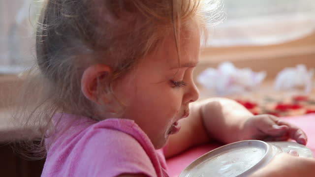 Side view of a playful little girl licking plate at the dinner table