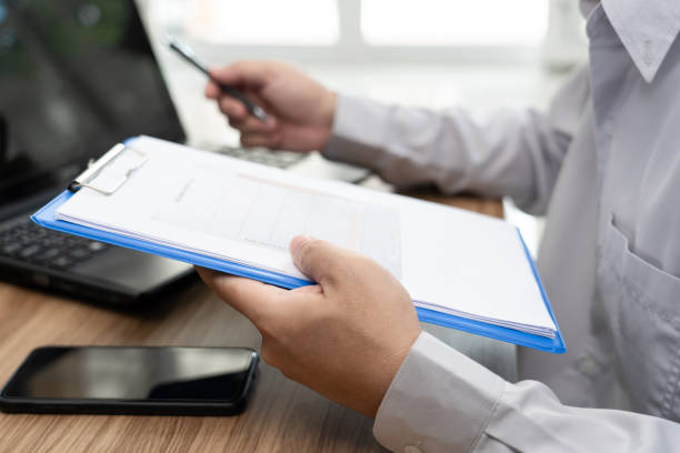 istock Close up hand a man hold graph data document and use laptop computer working online in office and smartphone on wood table 1340923782