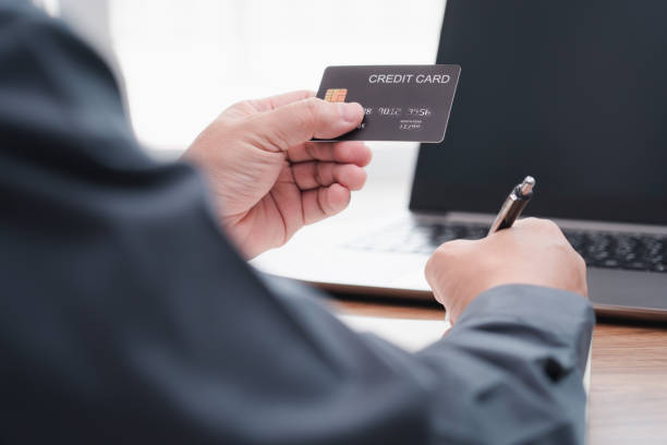 istock Businessman make online banking, making a payment or purchasing on the internet entering his credit card details on a smartphone and use laptop working on table 1340923808