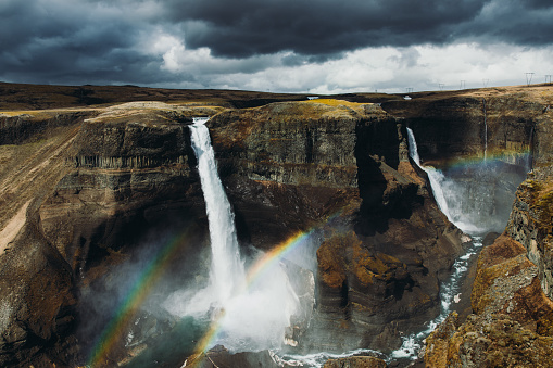 Dramatic view of the tall Haifoss waterfall in the canyon with colorful rainbow after the summer rain