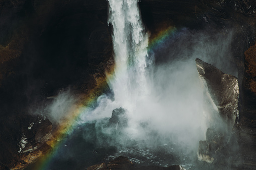 Dramatic view of the tall Haifoss waterfall in the canyon with colorful rainbow after the summer rain