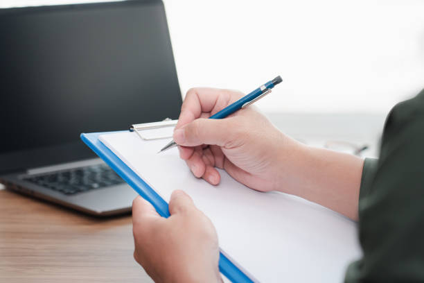 istock Car insurance staff writing on the white paper clip board file memory  insurance data form computer laptop glasses on table : car safety concept 1340928222