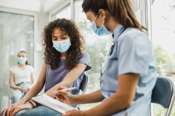 African American Girl Talking To Nurse Before Covid-19 Vaccine Nurse talking to African American female teenager and taking notes before vaccination against coronavirus. covid 19 patient stock pictures, royalty-free photos & images